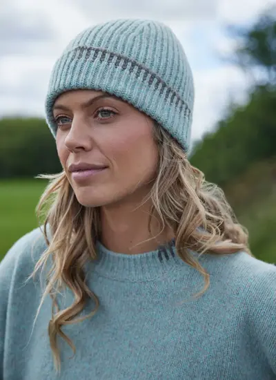 Woman wearing a ribbed Fisherman beanie in sea stone with contrast grey jacquard tipping, knit from merino wool and cashmere.